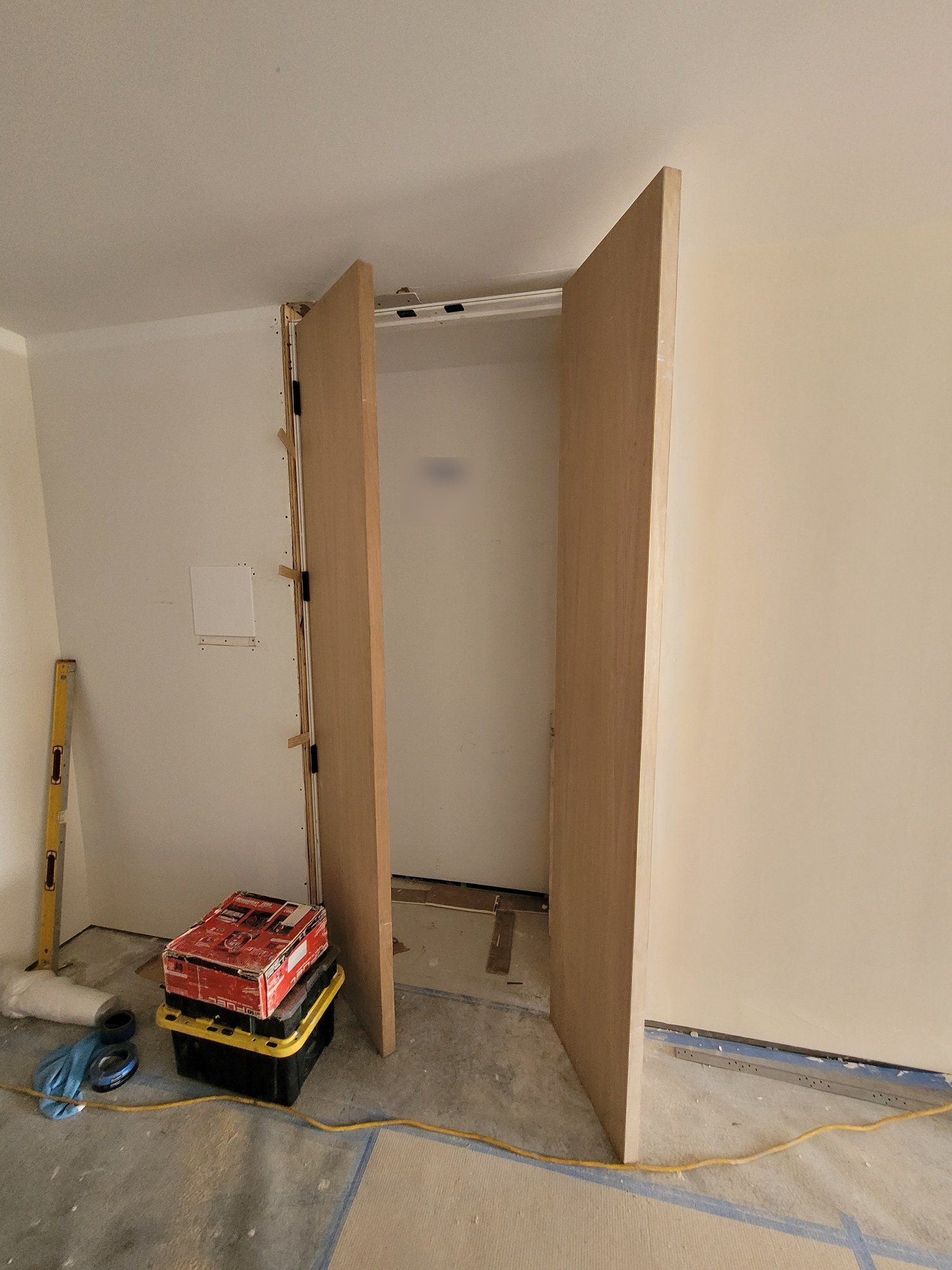 A pair of tall wood-veneer doors being hung at a closet opening.