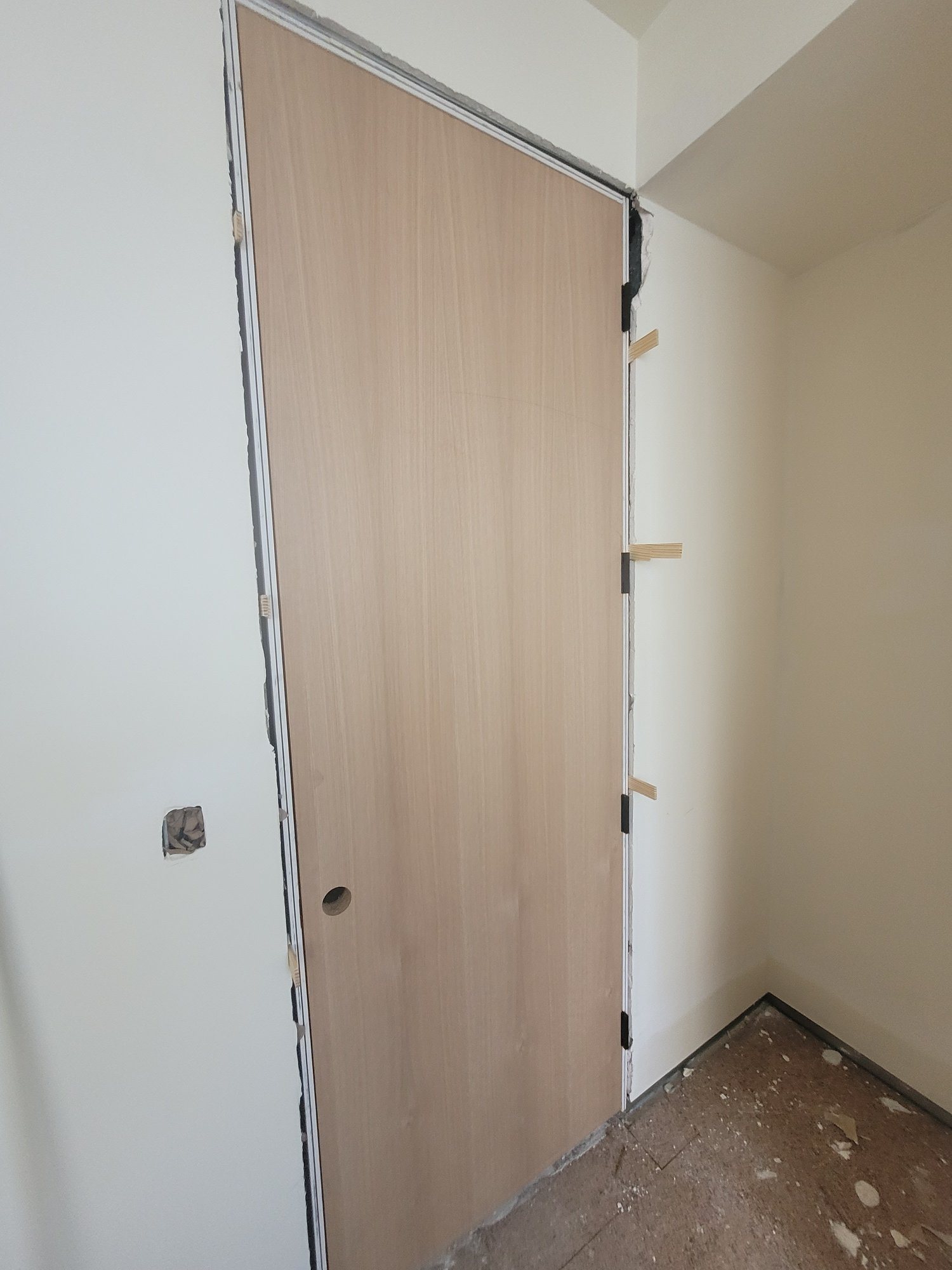 A flush wood-veneer door hung in a slim metal frame, shims still in place.