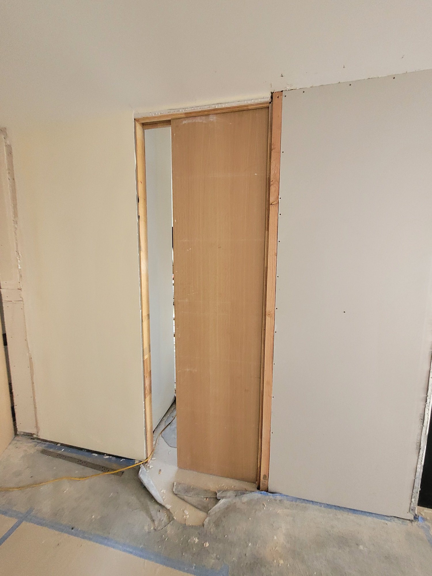 A wood-veneer pocket door sliding into a new drywall partition.
