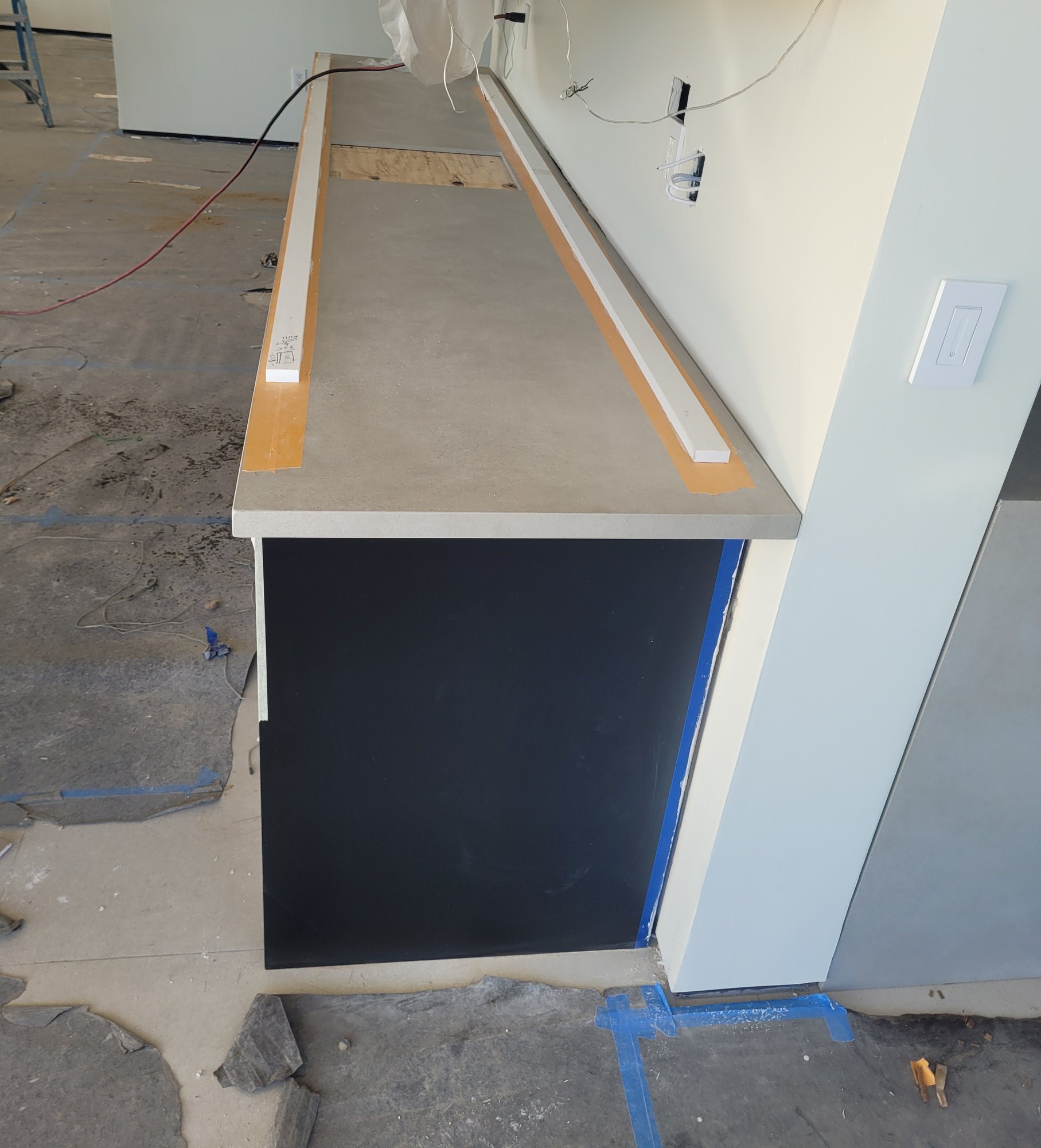 A countertop being set on a dark base cabinet, edges taped and the subtop showing at the sink cutout.