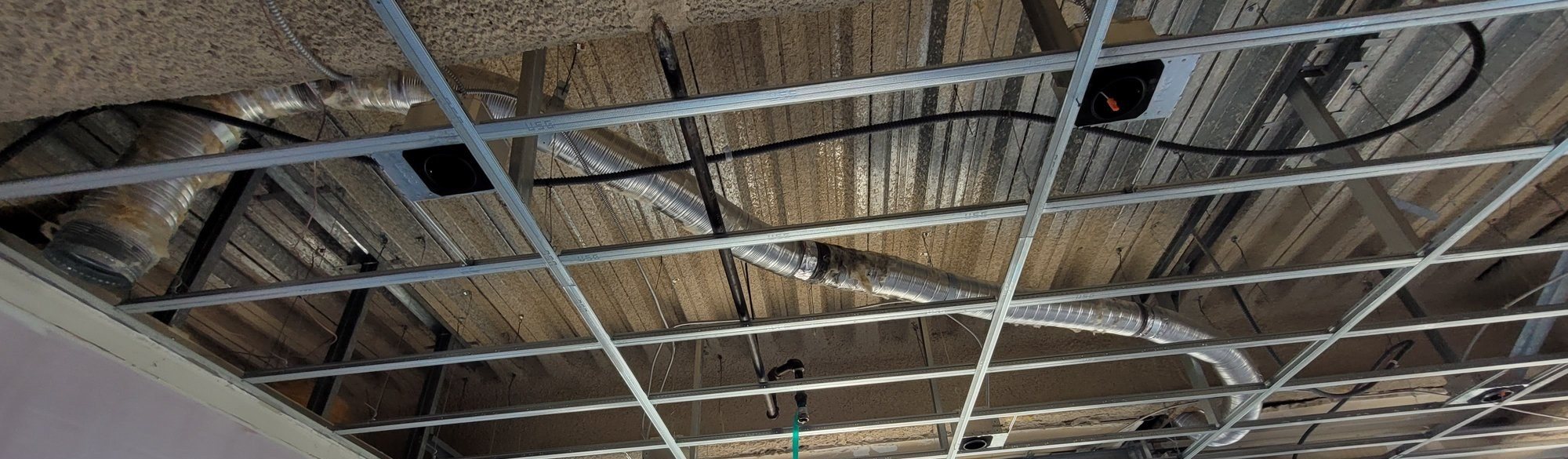 New metal ceiling grid hung below the concrete deck, with flexible duct and recessed light housings in place.