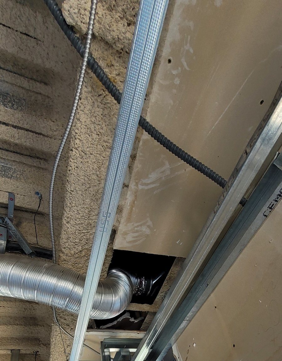 Ceiling framing at a soffit, with a flexible duct routed through a cut opening.