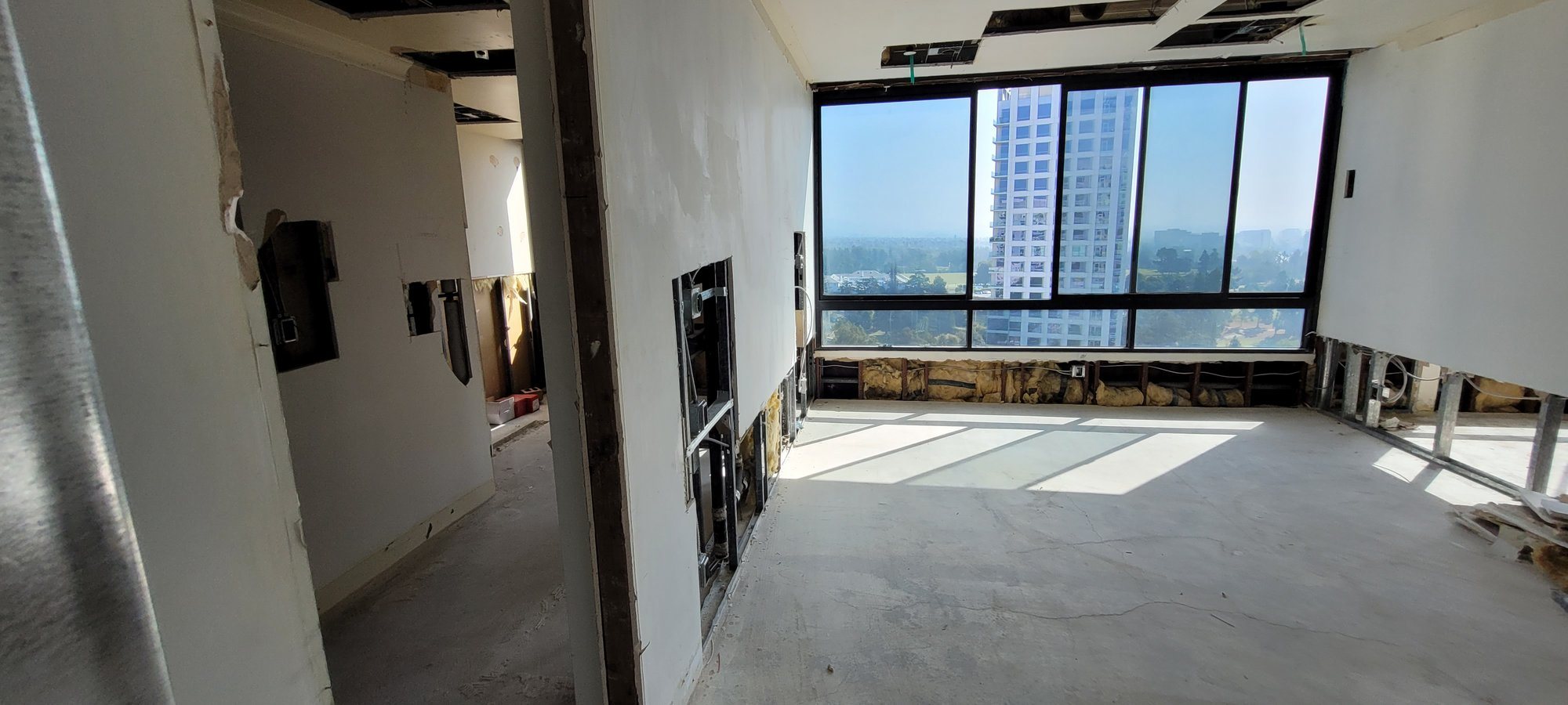 Empty living area on a bare concrete slab with the ceiling opened and lower walls cut away, below floor-to-ceiling windows