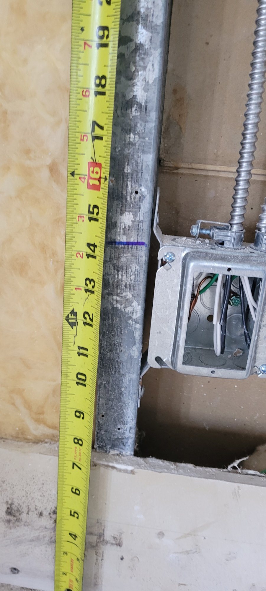 Measuring a low box height beside a steel stud, with insulation behind.