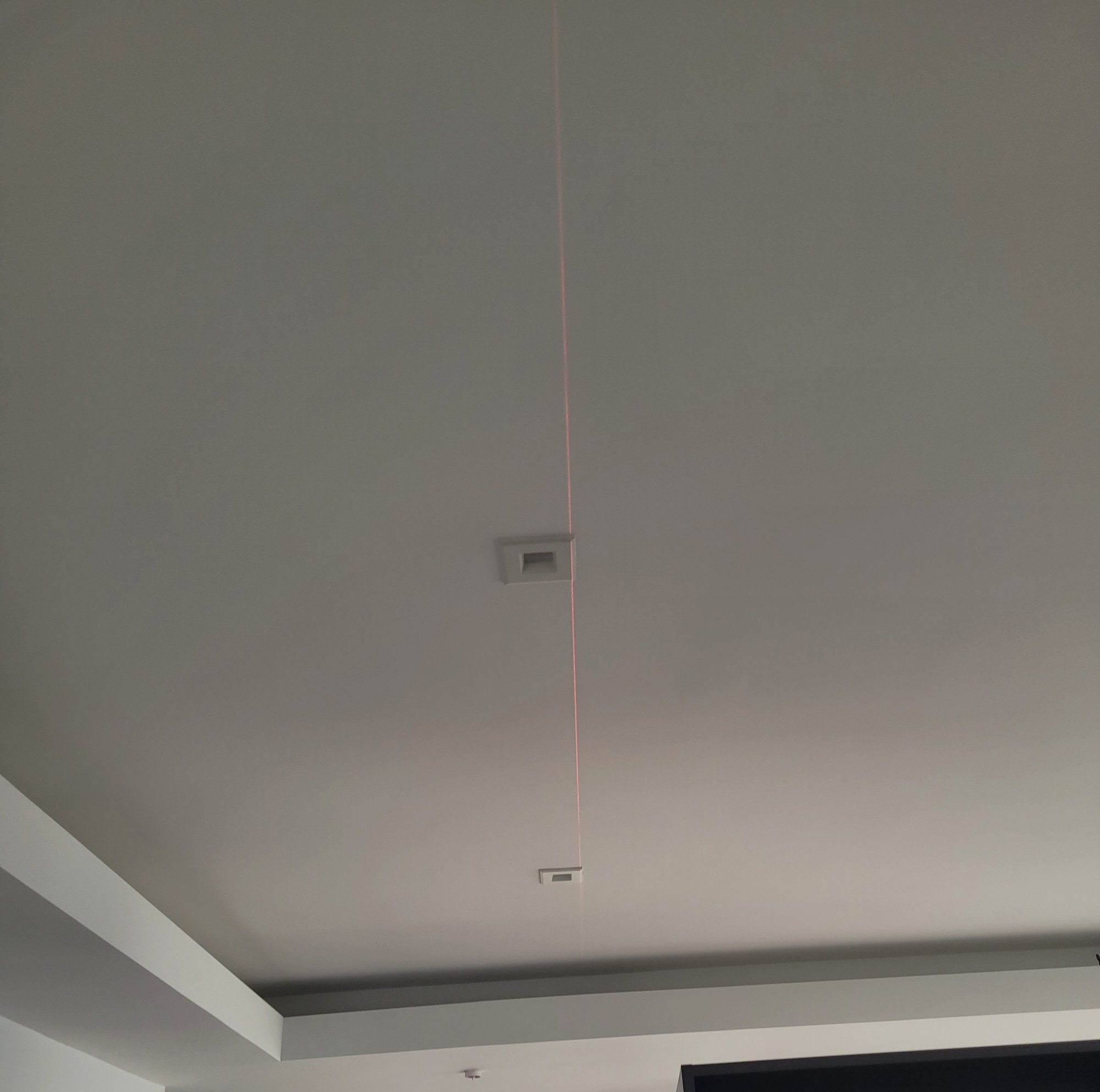 A laser line used to align recessed lights across a finished ceiling inside a stepped soffit.